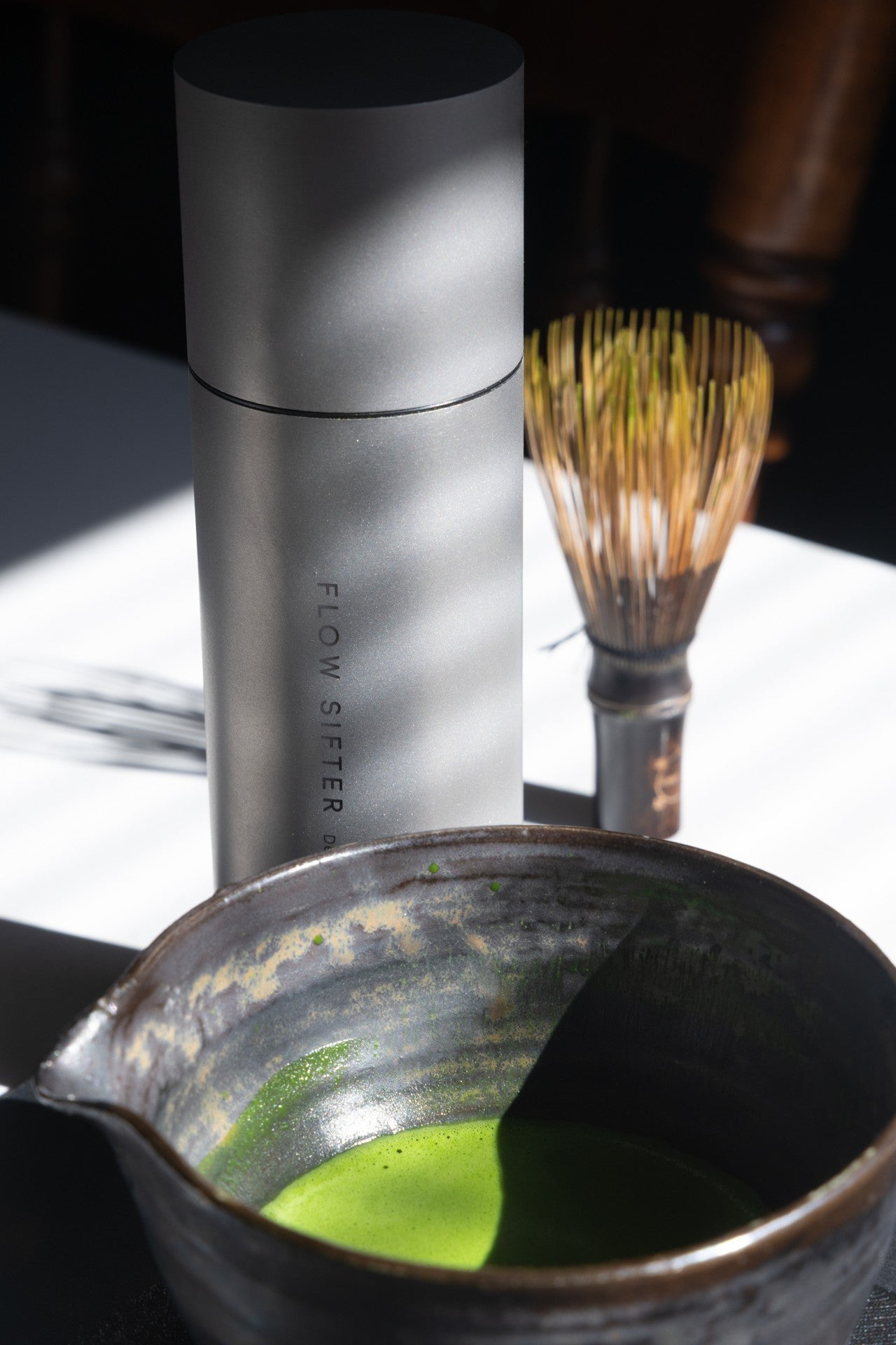Flow Sifter beside a bamboo whisk and a bowl of bright green matcha